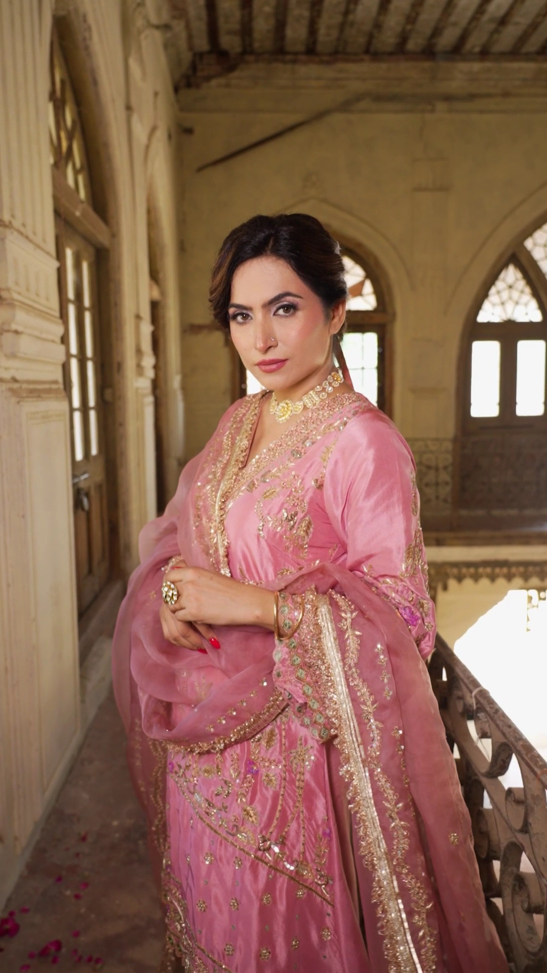 A woman wearing a pink embroidered outfit in a historic interior